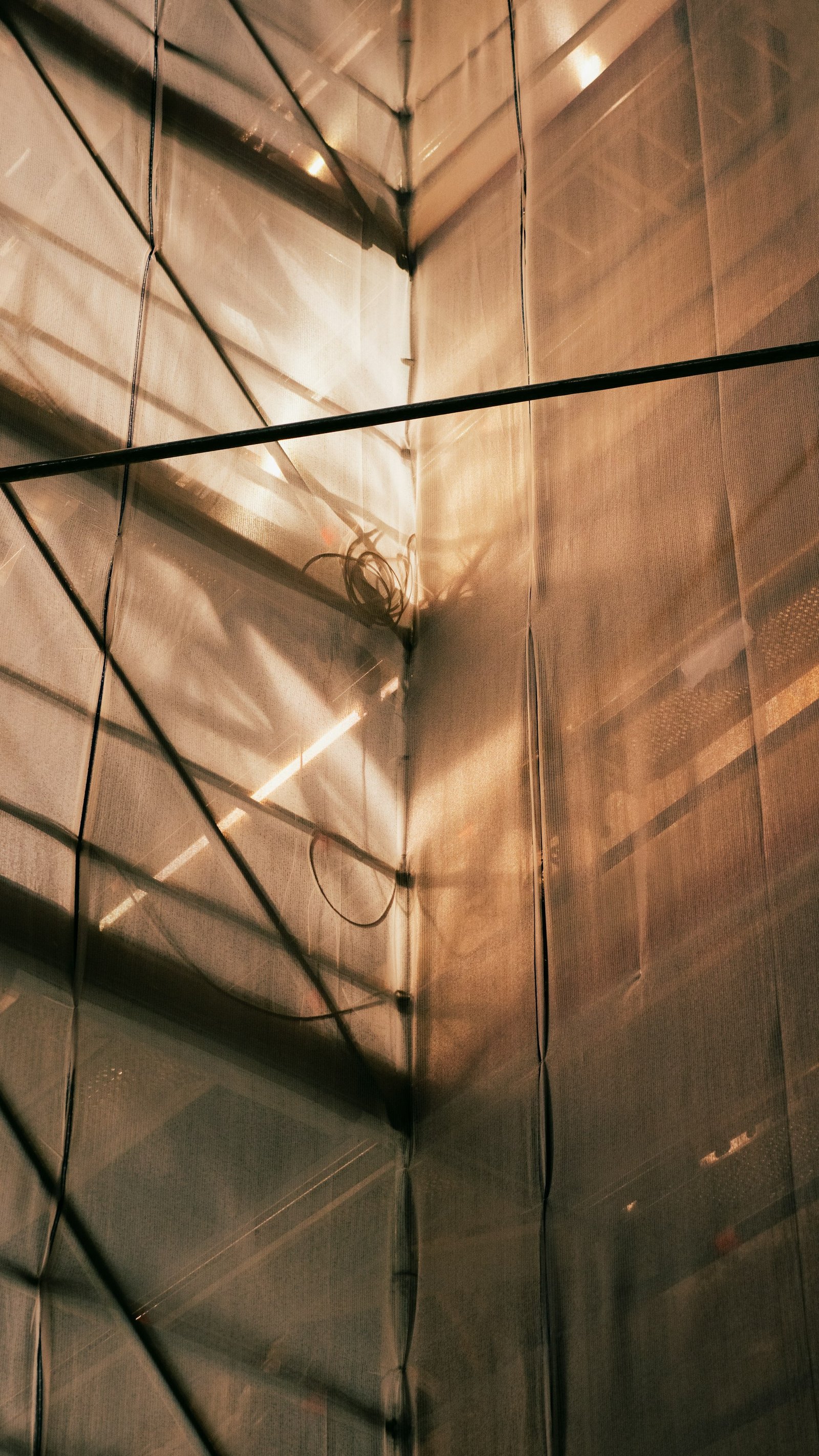 Scaffolding and construction sheeting crossed by warm light and shadow